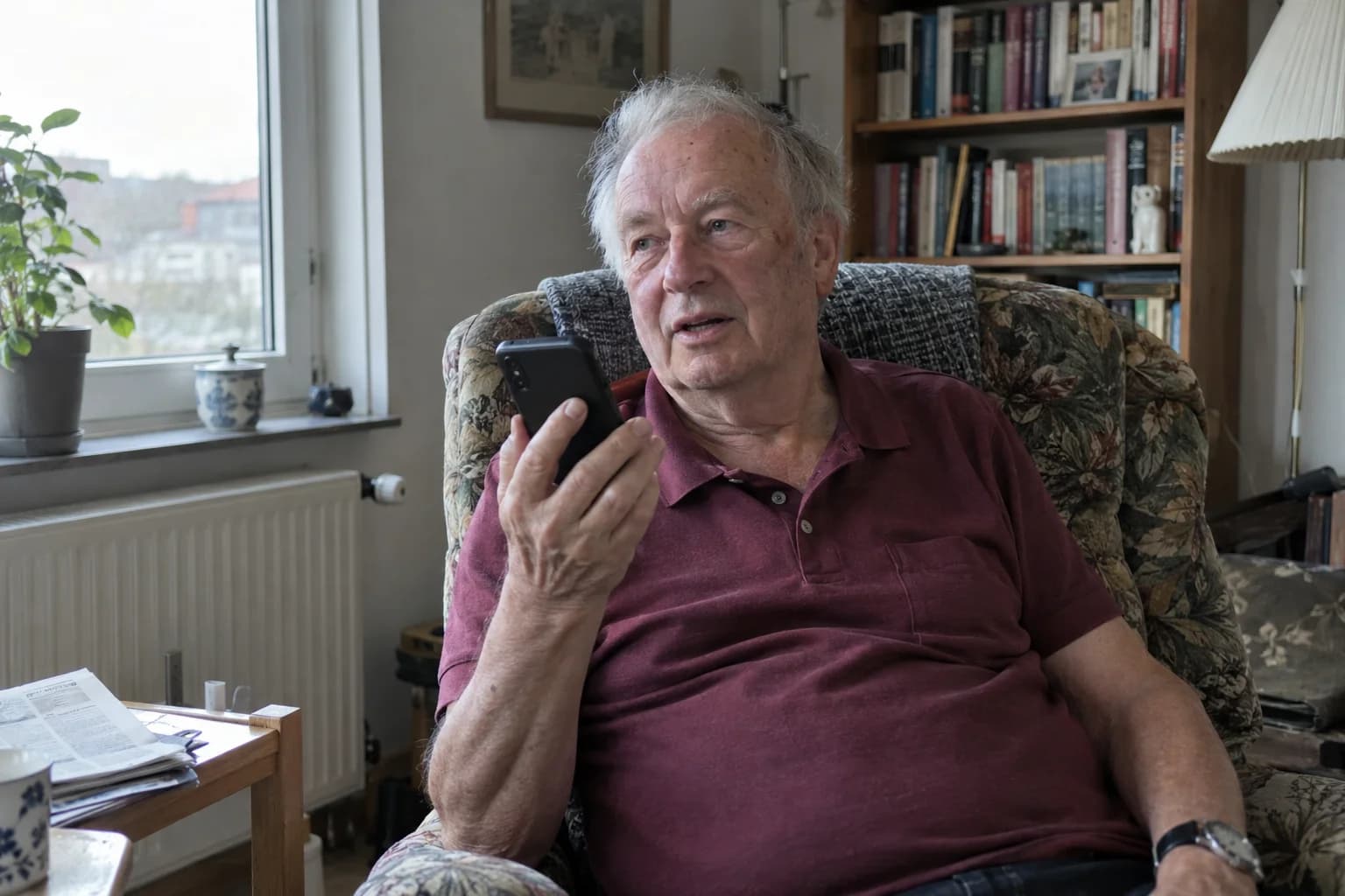 An older man in an armchair, talking to Elsy